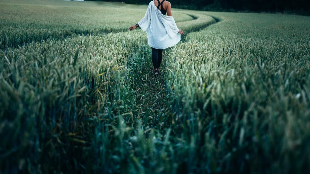 A serene image of a woman walking on a path through a lush wheat field in summer.